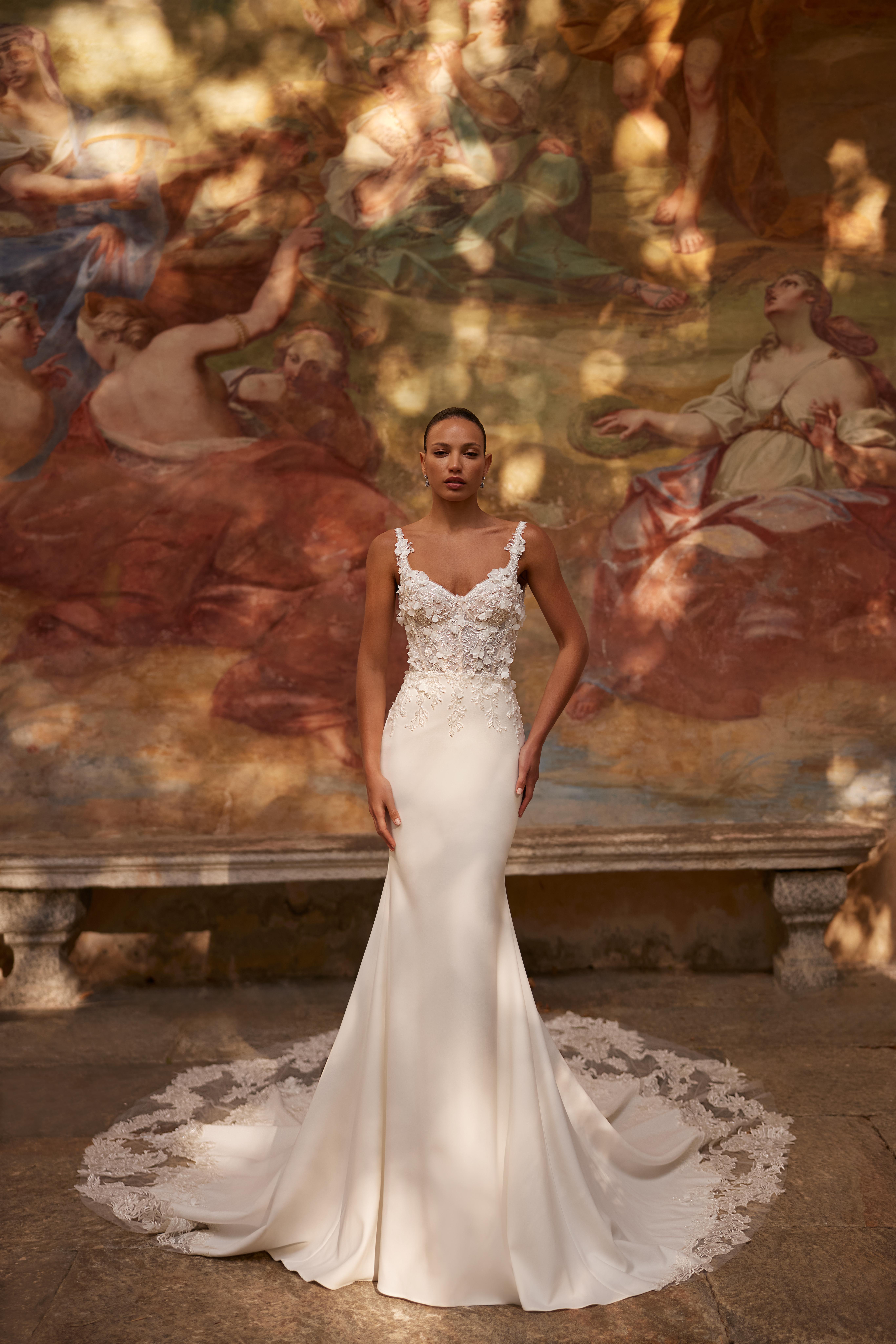 Женщина в свадебном платье с кружевными элементами на фоне художественной росписи.